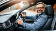 © Olga - A personable man in denim clothes is sitting at the wheel of a car and smiling