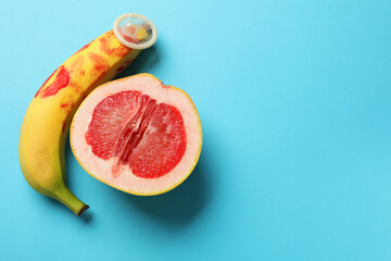 Wall Mural - Half of grapefruit, banana with condom and red lipstick marks on light blue background, flat lay with space for text. Safe sex concept