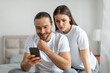 © Prostock-studio - Curious woman peering at man's smartphone screen
