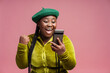 Stylish overjoyed African American woman holding mobile phone win money celebration success isolated on pink background. Happy Nigerian influencer communication online. Victory concept