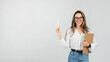 © Prostock-studio - A smiling young woman with glasses holding a clipboard and pointing up with a pen