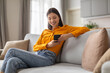 © Prostock-studio - Cheerful young woman enjoying smartphone on couch