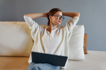 Wall Mural - Smiling woman using laptop on the couch in her modern home office She is a freelancer working on her startup, enjoying the comfort and convenience of working from home The room is filled with natural