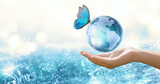 Fototapeta Kwiaty - Water Day or World Oceans Day concept. Environmental conservation, save, protect clean planet Earth and ecology, sustainable lifestyle. Globe and Morpho Butterfly in human hand on pure sea background.