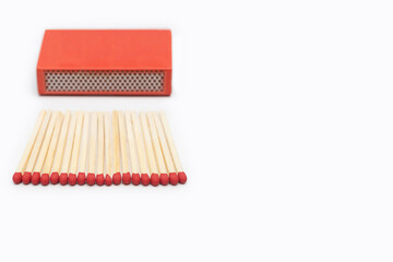 Matches near a red matchbox isolated on a white background. Matches and matchbox close-up with space for text. Red matches are laid out in an even row on a white background.