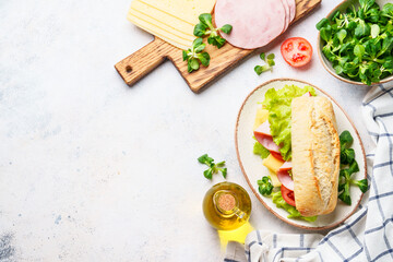 Canvas Print - Ciabatta sandwich with lettuce, cheese, tomatoes and ham on white table.