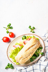 Canvas Print - Ciabatta sandwich with lettuce, cheese, tomatoes and ham on white table.