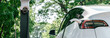 © Summit Art Creations - Panorama banner EV electric vehicle recharging battery from EV charging station in national park or outdoor forest scenic. Natural protection with eco friendly EV car travel in the summer woods. Exalt
