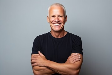 Wall Mural - Portrait of a happy senior man with arms crossed against grey background