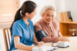 © chokniti - Medical health insurance service, Asian caregiver doctor examine older patient use blood pressure gauge. Young woman therapist nurse nursing home taking care to senior elderly woman