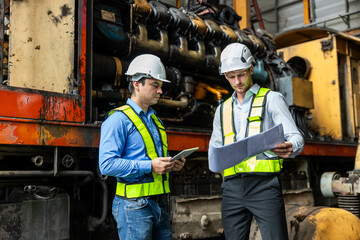 Wall Mural - Railway technician engineer wearing safety uniform and safety helmet holding tablet and blueprint check work plan standing at site railroad station. Locomotive repairman in factory.