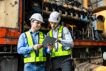 Wall Mural - Railway technician engineer wearing safety uniform and safety helmet holding tablet and blueprint check work plan standing at site railroad station. Locomotive repairman in factory.