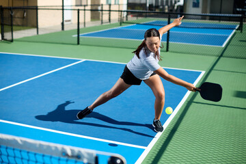 an asian girl plays pickleball on a blue court