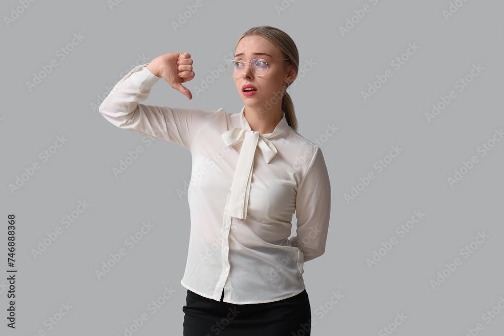Upset young businesswoman showing dislike on light background