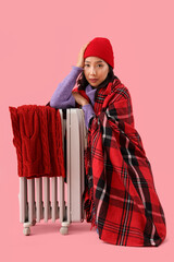 Sticker - Young Asian woman in winter clothes with radiator on pink background