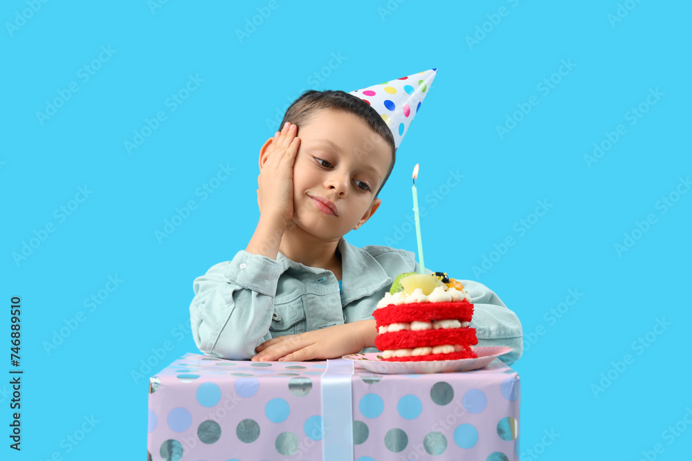 Cute little boy with Birthday cake and gift box on blue background