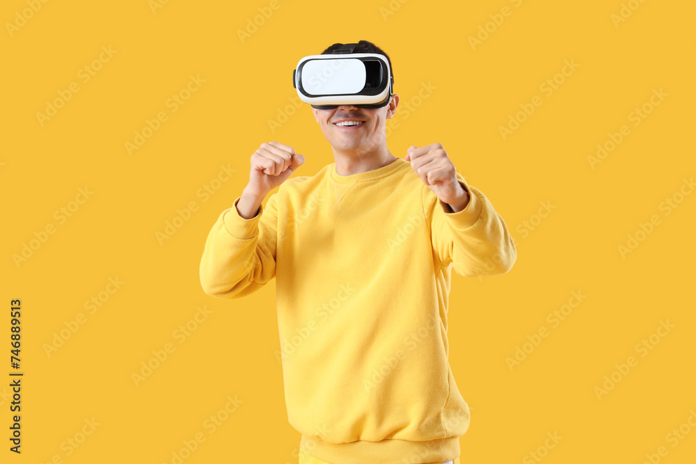 Young man in VR glasses on yellow background