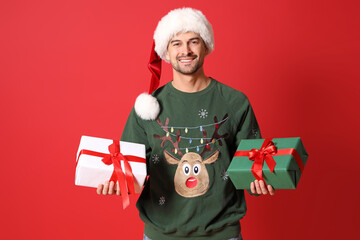 Sticker - Handsome man in Santa hat with Christmas gift boxes on red background