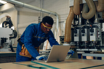 Contemporary Carpenter Working in factory, operating modern machines. Portrait of modern carpenter making wood furniture at industrial job site.