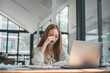 © Satori Studio - A fatigued female office worker massaging her eyes while working on a laptop in a bright office space.