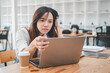 © Satori Studio - A young woman looks frustrated and stressed while concentrating on her laptop screen in a bustling cafe environment.