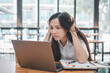 © Satori Studio - A young woman looks frustrated and stressed while concentrating on her laptop screen in a bustling cafe environment.