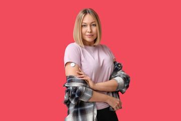 Wall Mural - Woman with glucose sensor for measuring blood sugar level on red background. Diabetes concept