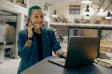 Fototapeta Panele - Stylish tattooed female business owner is use laptop while talking phone sitting in coworking
