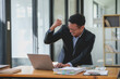 © amnaj - Happy asian businessman celebrating success with arms raised with laptop computer at office desk. Achievement and job satisfaction concept.