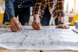 © Nuth - Using measuring tape and hard hats, professionals review and discuss construction blueprints carefully around a worktable, focused on their work.