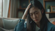 mulher asiática deprimida sentada no sofá da sala em casa sentindo dor de cabeça