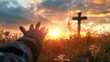 © tashechka - A person's hand reaching out towards the sun during a vibrant sunset with a cross in the background.