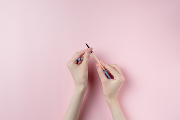 Wall Mural - Eyeliner in hand on pink background, top view