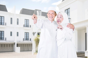 Wall Mural - Happy Muslim old man embracing his wife while looking and pointing