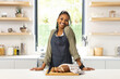 A young African American woman stands with a confident smile in a bright kitchen
