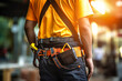 A man wearing a yellow shirt is holding a tool belt