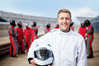 © Connect Images - Smiling racer holding helmet with team in background at the track.