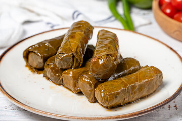 Wall Mural - Stuffed grape leaves with olive oil. Dolma prepared with grape leaves and rice. Stuffed grape leaves or dolmades with olive oil on a white wooden background. local name yaprak sarma. Close up