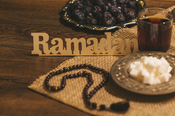 Wall Mural - Glass of tea with sugar and dried dates on a wooden background with burlap. Ramadan Kareem holiday background. Halal meal set for fasting is obligatory for Muslim on wooden.  Soft focus. Shallow DOF.