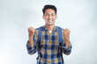 Excited young Asian man student wearing flannel shirt with backpack making winner gesture and celebrating success isolated on white background. Education in high school university college concept