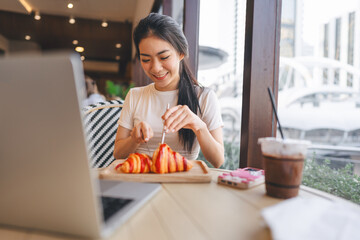 Wall Mural - Happy smile asian woman eating bread at cafe sitting near window indoors on day