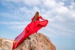© svetograph - woman sky red dress. Woman with long hair on a sunny seashore in a red flowing dress, back view, silk fabric waving in the wind. Against the backdrop of the blue sky and mountains on the seashore.