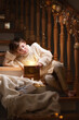 Boy kid sitting with with a fabulous box and gifts near to the stairs in Christmas. New Year, happiness and fairy tale