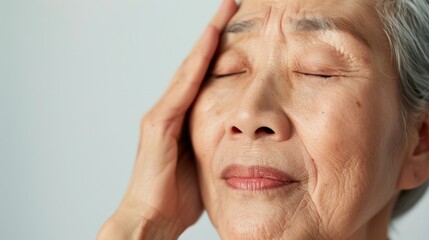 Wall Mural - An elderly person with closed eyes resting their hand on their forehead possibly in a state of relaxation or contemplation.