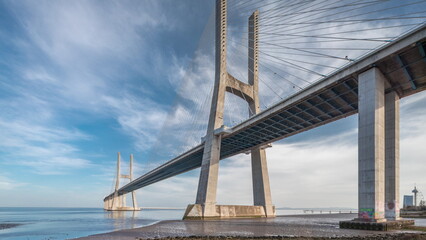 Wall Mural - Vasco da Gama bridge timelapse hyperlapse with water in river and blue cloudy sky. Lisbon, Portugal.