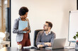 © dusanpetkovic1 - A manager is sitting at the office while an african american businesswoman is standing next to him and reporting.