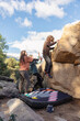 © ADDICTIVE STOCK - Three friends engage in bouldering on a rocky mountain, with one scaling the boulder and two spotting for safety on a crash pad