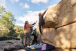 © ADDICTIVE STOCK - Three friends engage in bouldering on a rocky mountain, with one scaling the boulder and two spotting for safety on a crash pad