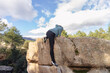 © ADDICTIVE STOCK - Anonymous climber reaches the summit of a large boulder, set against a backdrop of pine trees and mountainous landscape