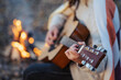Close up of a girl playing the guitar near bonfire. Playing the guitar outdoors on nature, having good time with friends near the fire